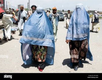 Two women in a Kabul street wear the customary blue burqas that hide their faces but partly reveal modest dress beneath Stock Photo