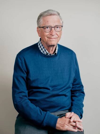 A portrait of Bill Gates, who is wearing a blue crew neck sweater over a plaid white and blue shirt. He is looking at the camera with a hint of a smile. 