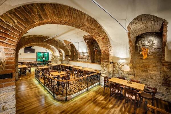 Restaurace s dřevěnými stoly a židlemi a cihlovými zdmi.