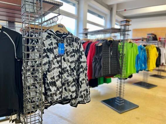 Innenansicht des Daiber Factory Outlet Ladengeschäfts: Verkaufsfläche mit zahlreichen Sport- und Outdoor-Kleidungsstücken, die an Kleiderständern und Regalen präsentiert werden.