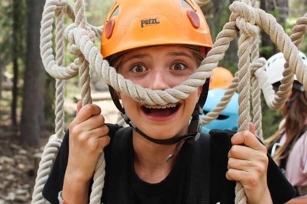 A camper smiles happily at summer camp while looking through a cargo net