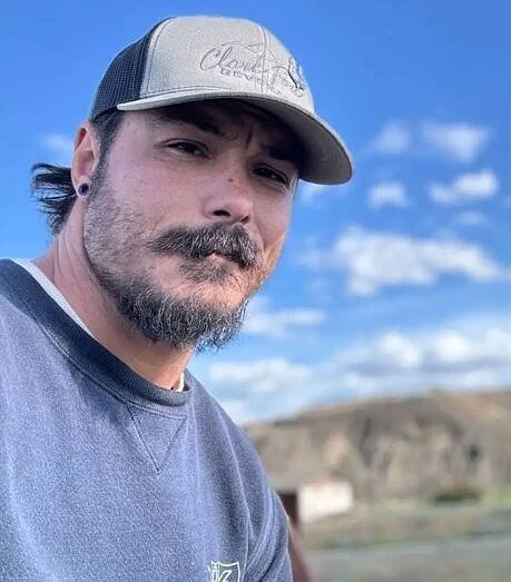Man with beard and cap outdoors under blue sky, related to blood not belonging to a human found at fugitive dad crime scene
