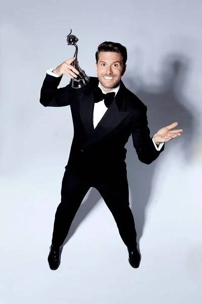 Man in tuxedo holding award.
