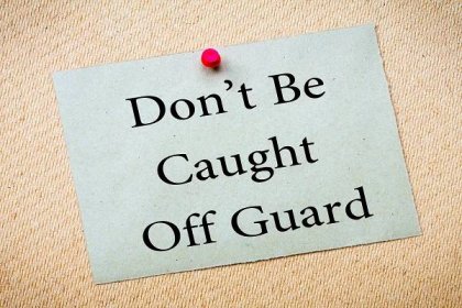DON'T BE CAUGHT OFF GUARD Message. Recycled paper note pinned on cork board. Concept Image