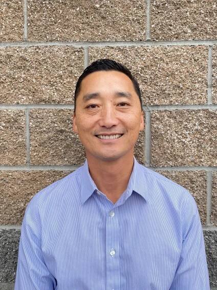 A man in a blue striped shirt is smiling in front of a brick wall.