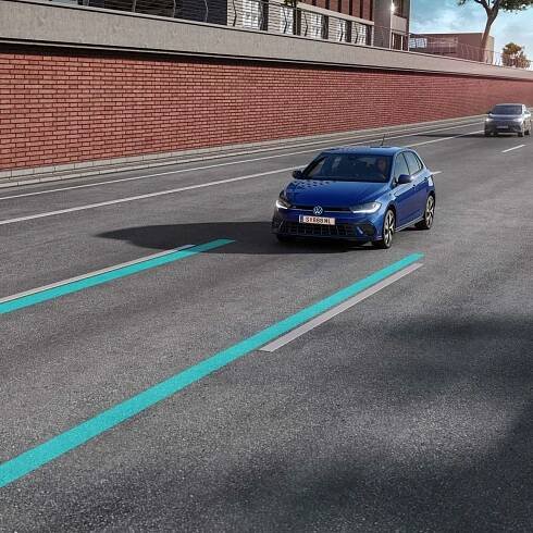 Znázornenie asistenčného systému jazdy Lane Assist pri modeli VW Polo. Vozidlo jazdí po mestskej diaľnici. Za ním je ďalšie auto. V pozadí vidieť mestské budovy.