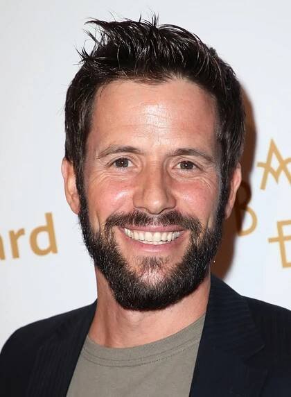 Christian Oliver wears a gray shirt with a black jacket