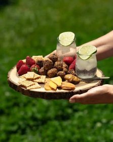 Hand holding a wooden cutting board full of snacks and fresh water, showcasing a snack option for picky eater