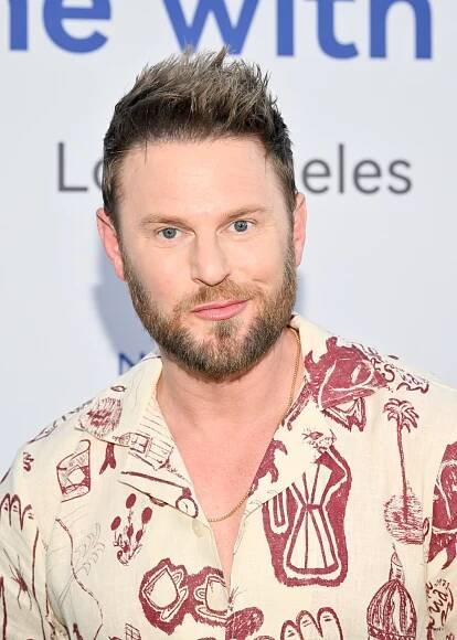 A person wearing a patterned shirt poses for a photo at a celebrity event