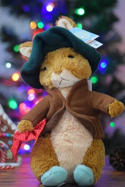Benjamin plushie siting in front of a pre-lit Christmas tree.