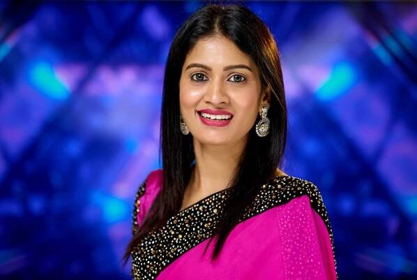 Woman in pink and gold sari poses against blue backdrop.