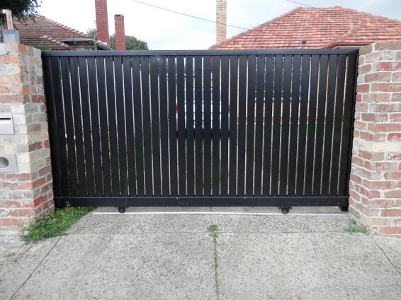 an iron gate in front of a brick wall with grass growing on the ground below