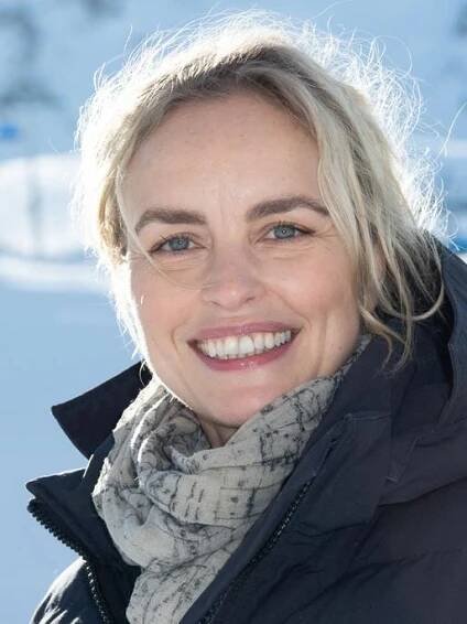 Nina Hoss steht freundlich lachend in einer Schneelandschaft