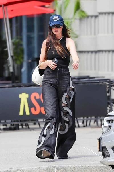 A woman wearing stylish clothing and a cap walking on a sidewalk