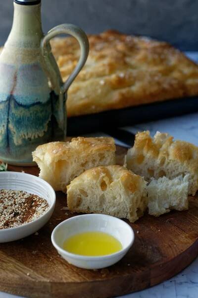 Focaccia slices on wood plate with bowl of oil and dukkah to show serving suggestion. 