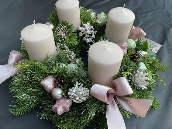 a wreath with white candles and greenery on a black tablecloth covered table cloth