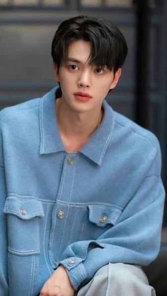 a young man sitting on the ground wearing a blue jacket
