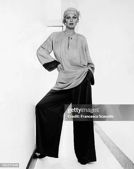 Italian actress Dalila di Lazzaro, standing in a narrow hallway, wearing a cashmere/silk tunic over satin crepe de chine pants by Geoffrey Beene.