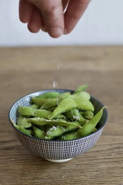 Mit den Fingern Salz auf die Edamame streuen