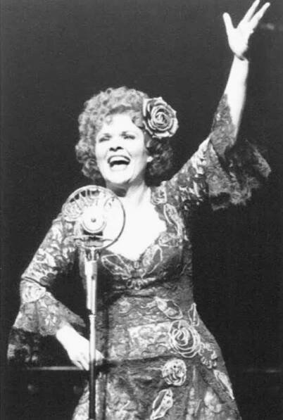 Black and white photo of Debra Monk singing "Everybody’s Girl" in Steel Pier. She stands at the microphone singing with an open mouth, one hand on her hip, and one hand raised.