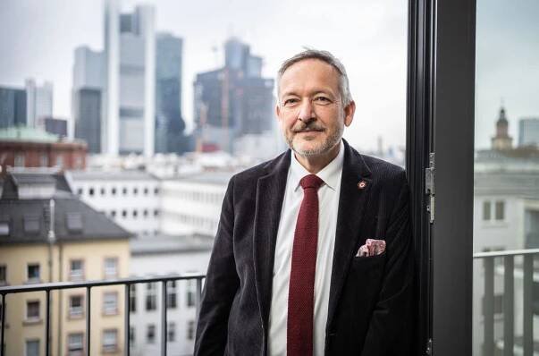 Peter Kraus vom Cleff steht vor dem Fenster seines Büros. Durch das Fenster erkennt man die Skyline von Frankfurt am Main.