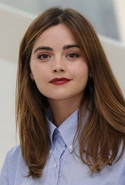 a woman with long brown hair wearing a blue shirt and red lipstick is looking at the camera