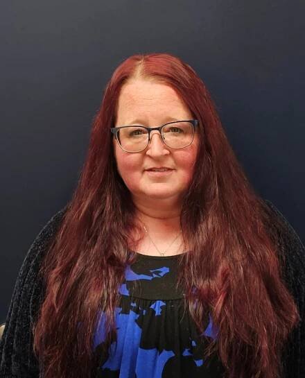A woman with long red hair and glasses is wearing a blue and black dress.