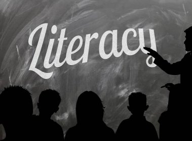 person in front of class with 'literacy' on chalk board