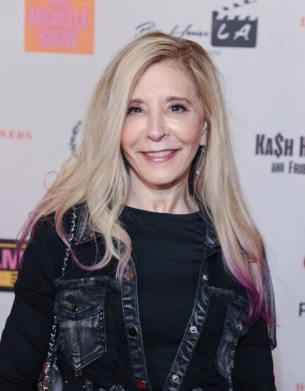 A woman with blond hair and purple highlights smiles for the camera in front of a branded backdrop.