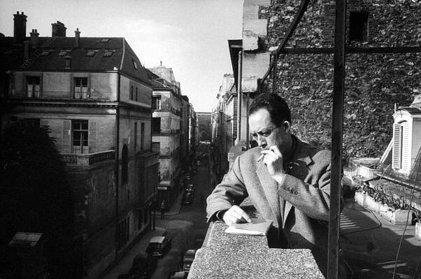 Albert Camus fumant une cigarette sur un balcon chez son éditeur en 1955.