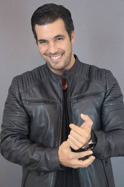 a man in a black leather jacket holding a wine glass and smiling at the ...