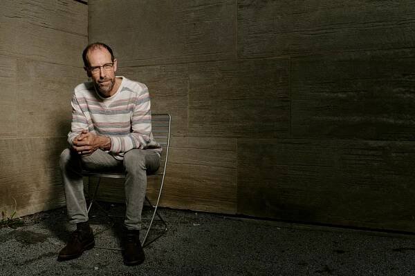 David Keith sitting on a folding chair with his hands clasped. 