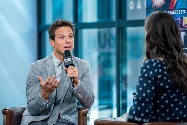 Scott Wolf in a silver suit with a microphone in his left hand