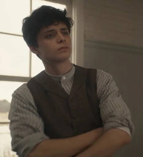 a young man with his arms crossed standing in front of a window