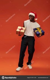 Download - Full length of jolly african american man in casual clothes and santa cap holding gift boxes on red — Stock Image