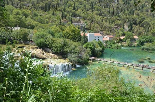 Looking down on the waterfalls and people swmming at it and walking on the bridge