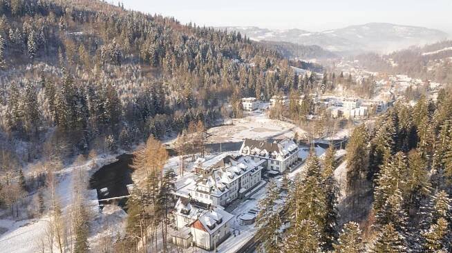 Aries Hotel & Spa Visla Exteriér fotografie An aerial shot captures a picturesque winter scene in a mountainous region. The foreground is dominated by a snow-covered landscape with a river winding through it. The riverbanks are lined with snow-laden trees, and a small bridge spans the water. 
