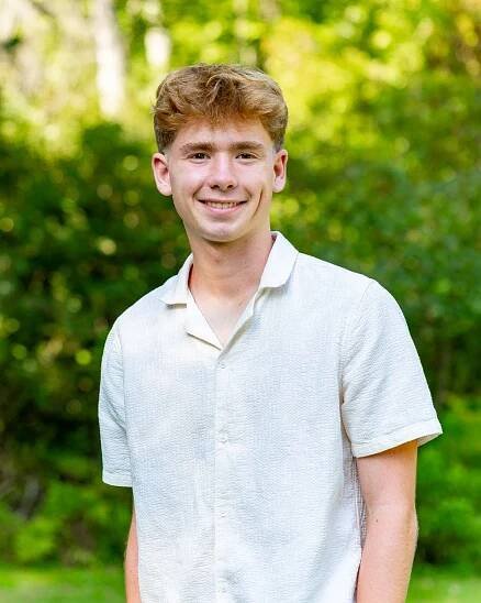 Teen boy poses at his High School Senior portrait photo session with autumn foliage in the background at home in Maynard, Massachusetts.