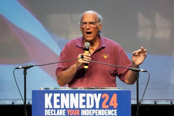 Jesse Ventura holds a microphone and speaks at a lectern that reads, Kennedy 24.