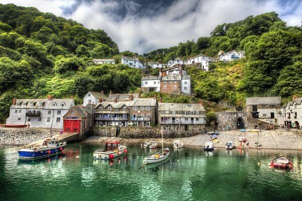 Clovelly fishing port in Devon, with houses on a hillside overlooking a harbor filled with boats.