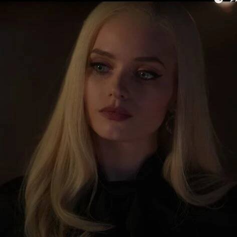a woman with blonde hair and blue eyes looks into the distance in a dark room