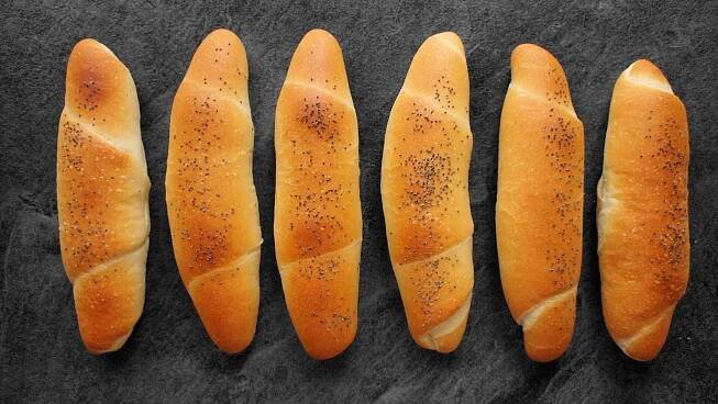 four loaves of bread lined up in a row on a black surface with sprinkled seeds