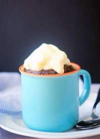chocolate mug cake topped with whipped cream, in a blue mug with a tablecloth in the background