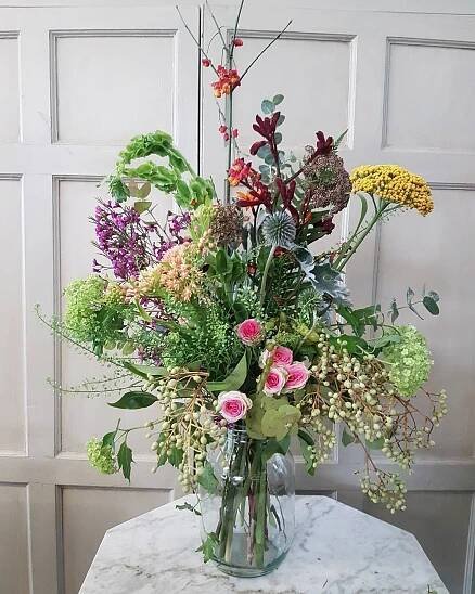 a vase filled with lots of flowers on top of a marble table next to a wall