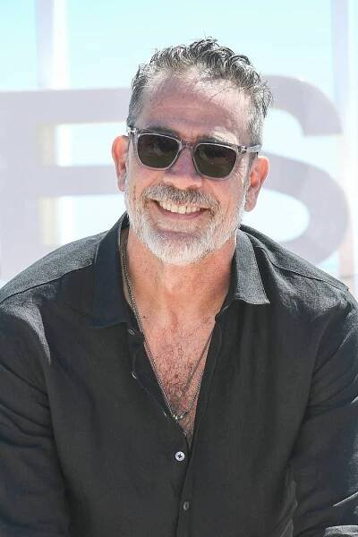 Jeffrey Dean Morgan with beard and sunglasses, wearing an open-collared shirt, smiles outdoors