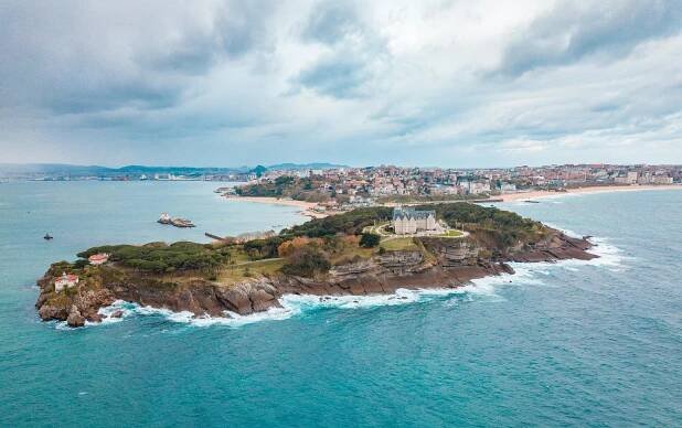 magdalena peninsula from a distance looking back over it from the ocean at the height of a drone with waves crashing to the cliff side edges of the peninsula. The peninsula has so many different things to do in santander on it.