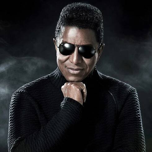 Portrait photo de Jermaine Jackson, posture affirmée et fond mystérieux.
