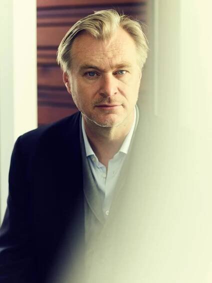 A blond man in a dark blazer looks through a reflective panel of glass