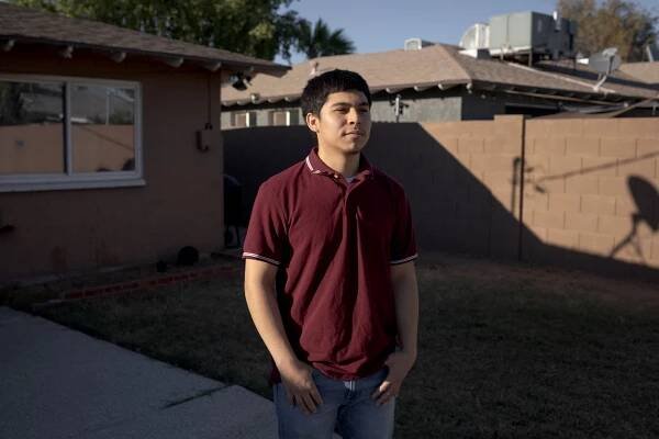 Miguel Gomez, dressed in a polo shirt and jeans, stands outside his home in Phoenix.