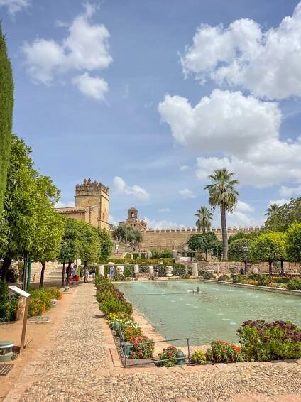 gardens with a long fountain that looks liek a swimming pool and a castle in the background at the alcazar which is one of the best things to do in cordoba.